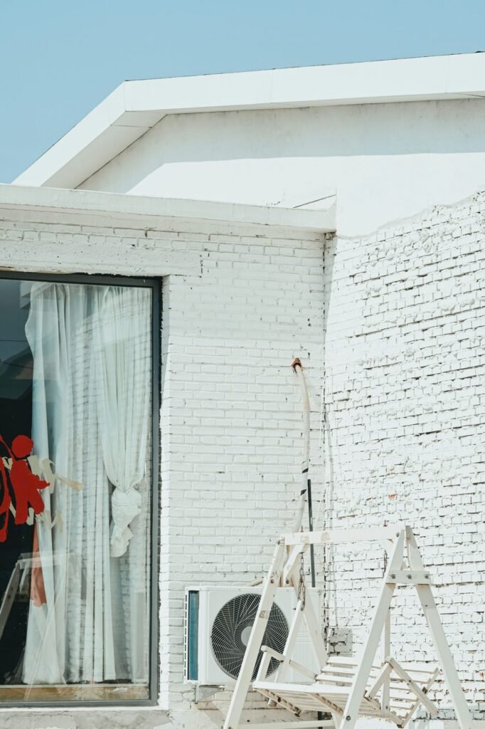 Outdoor air conditioning unit beside a white brick house during installation.