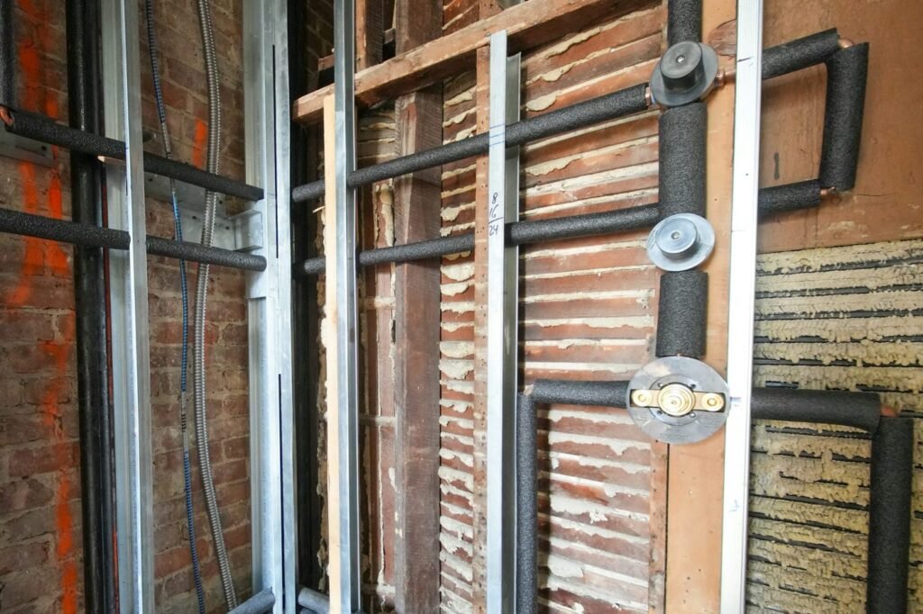 Insulated water pipes and shower valve connections exposed inside an unfinished wall