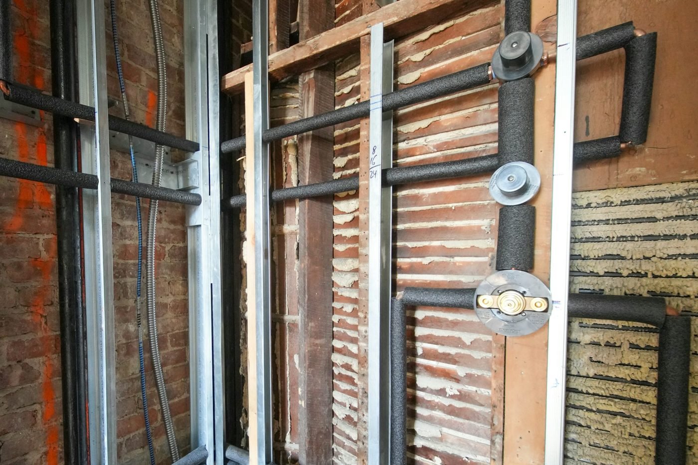 Insulated water pipes and shower valve connections exposed inside an unfinished wall