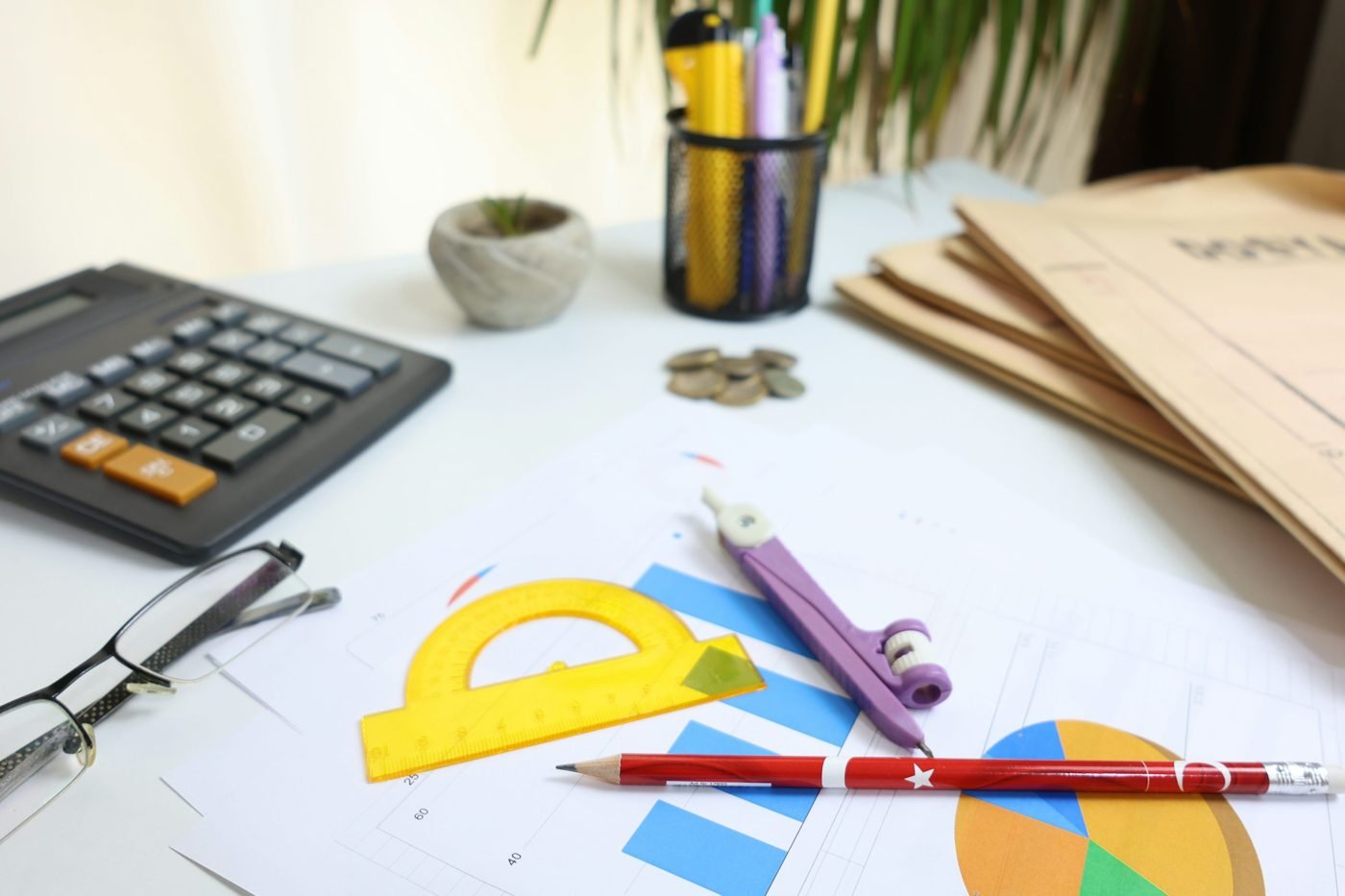 Calculator, coins, glasses and drawing tools on printed charts at a desk