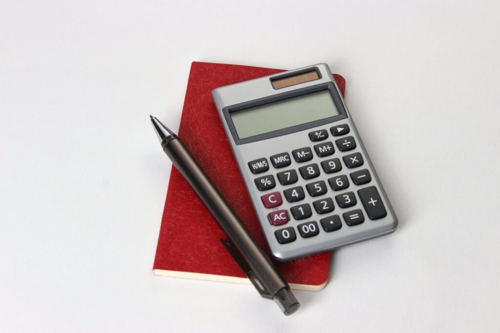 Calculator and black pen resting on a red notebook