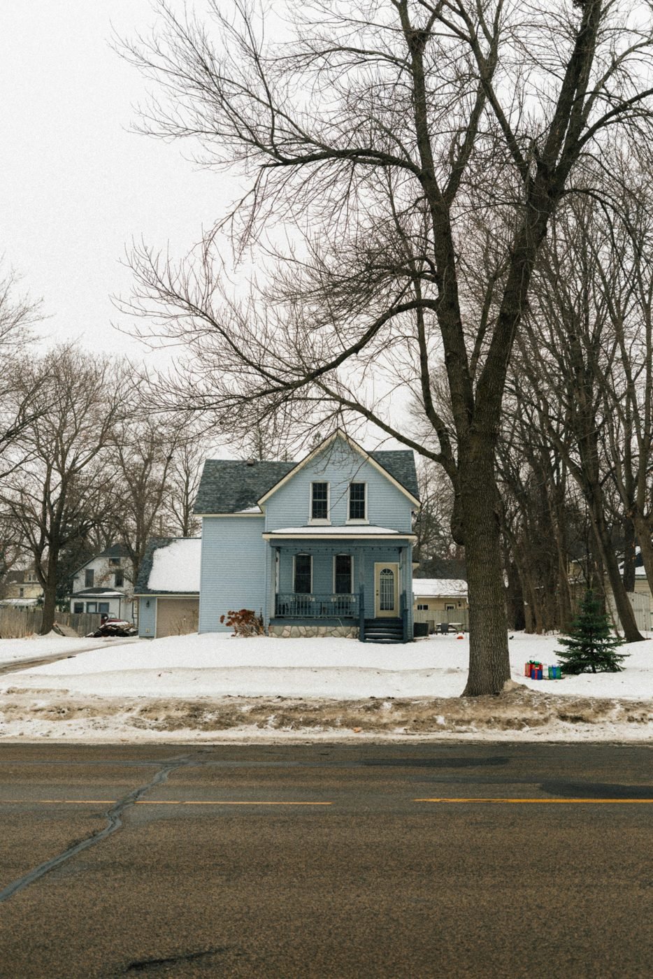 Light blue house on a snow-covered residential street.