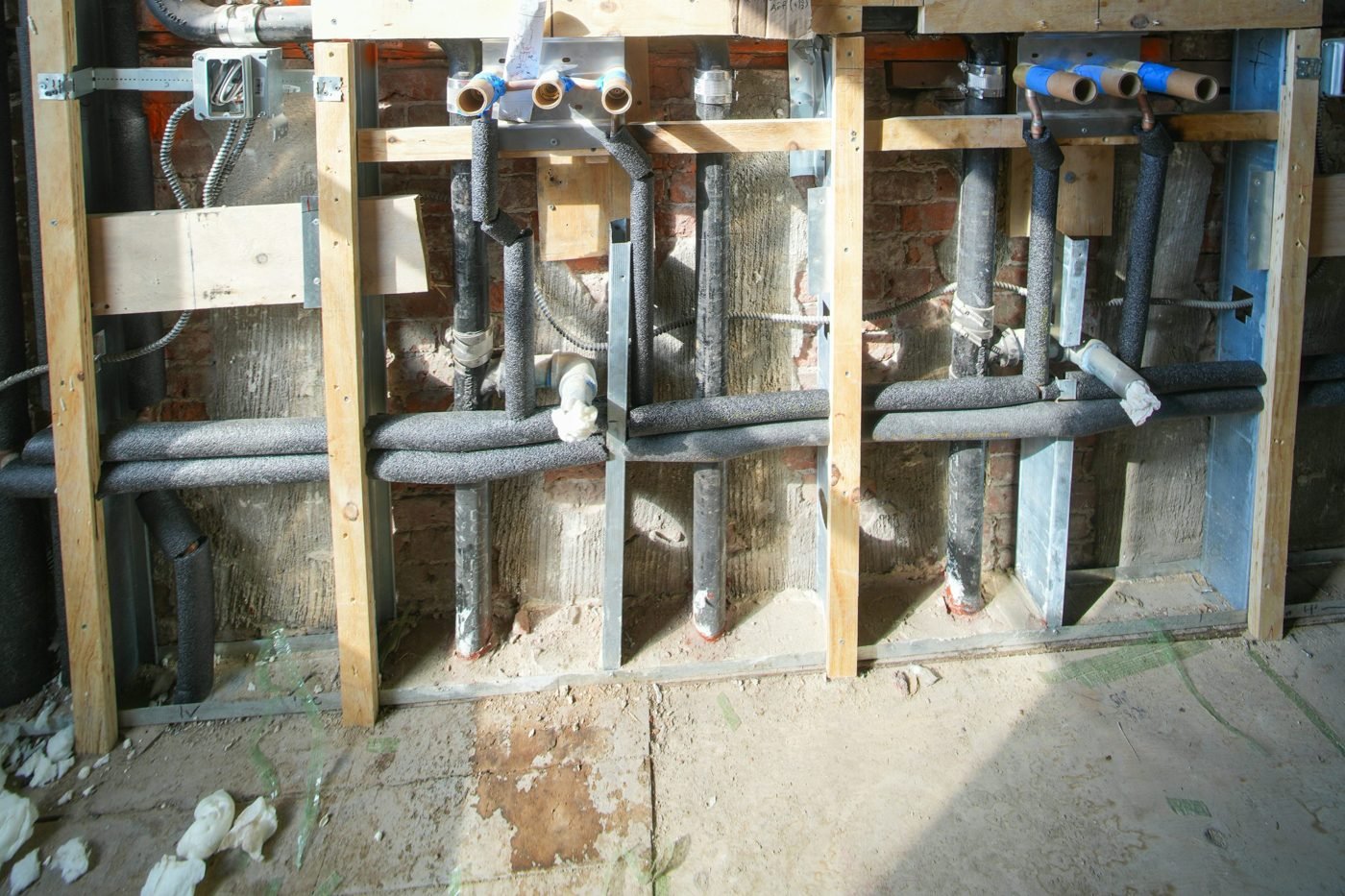 Insulated plumbing pipes and electrical conduit exposed between wall studs during renovation
