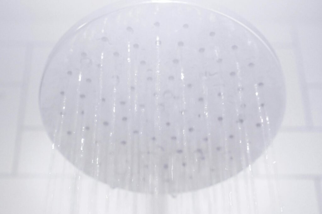 Water flowing from a round shower head in front of a tiled wall