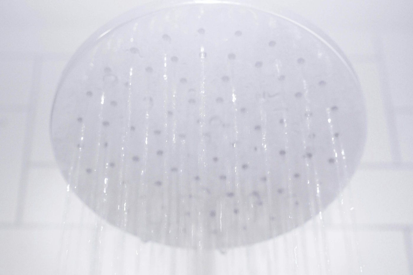 Water flowing from a round shower head in front of a tiled wall