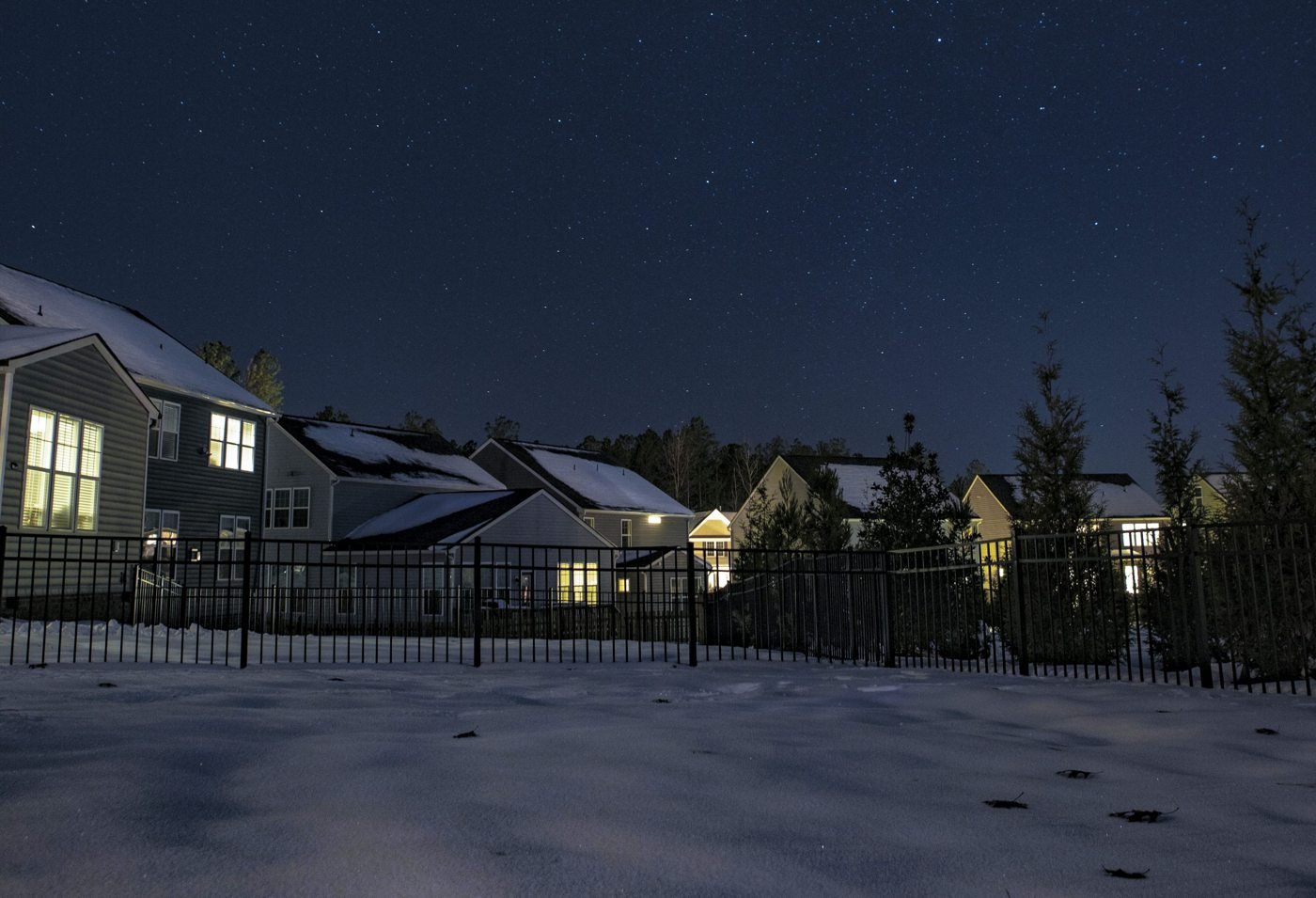 Snow-covered homes with lit windows beneath a night sky.