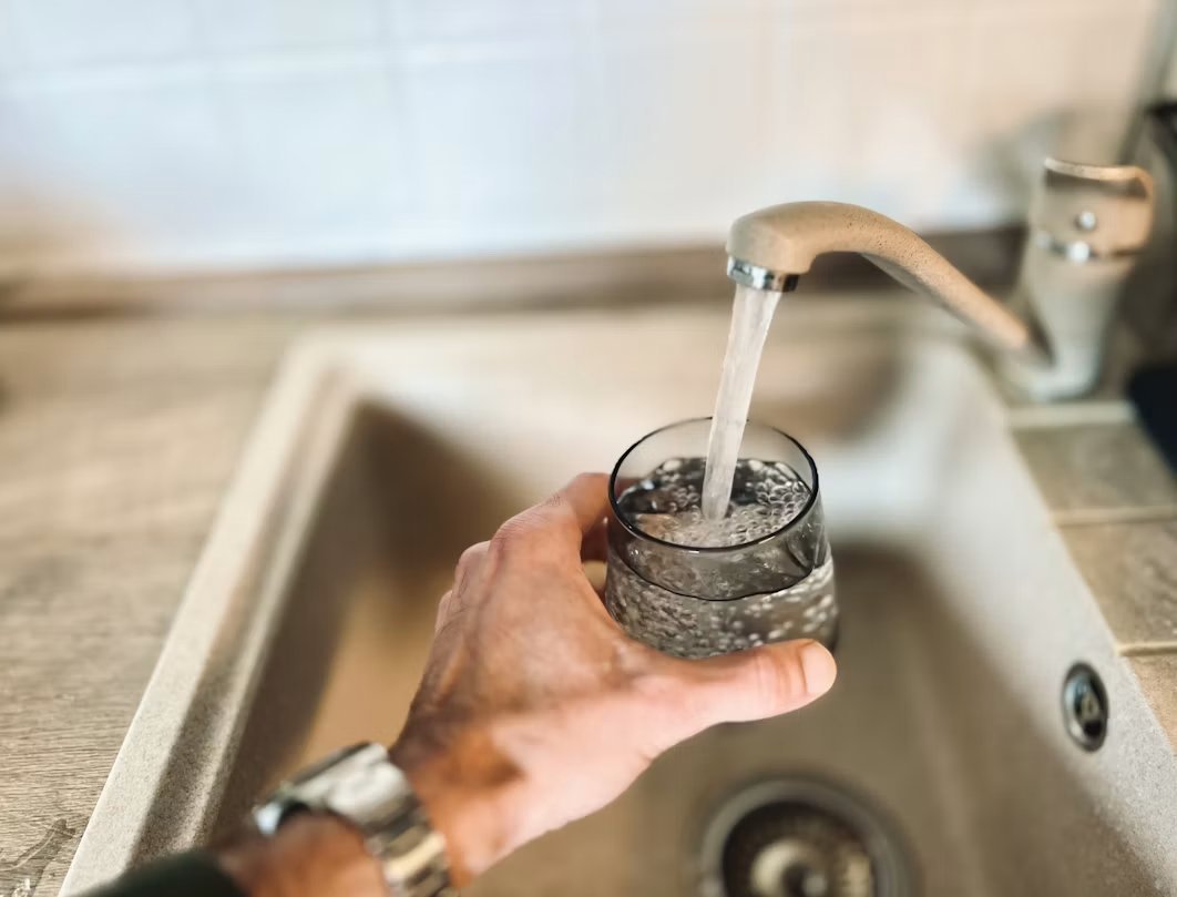 Hand filling a drinking glass from a kitchen faucet.