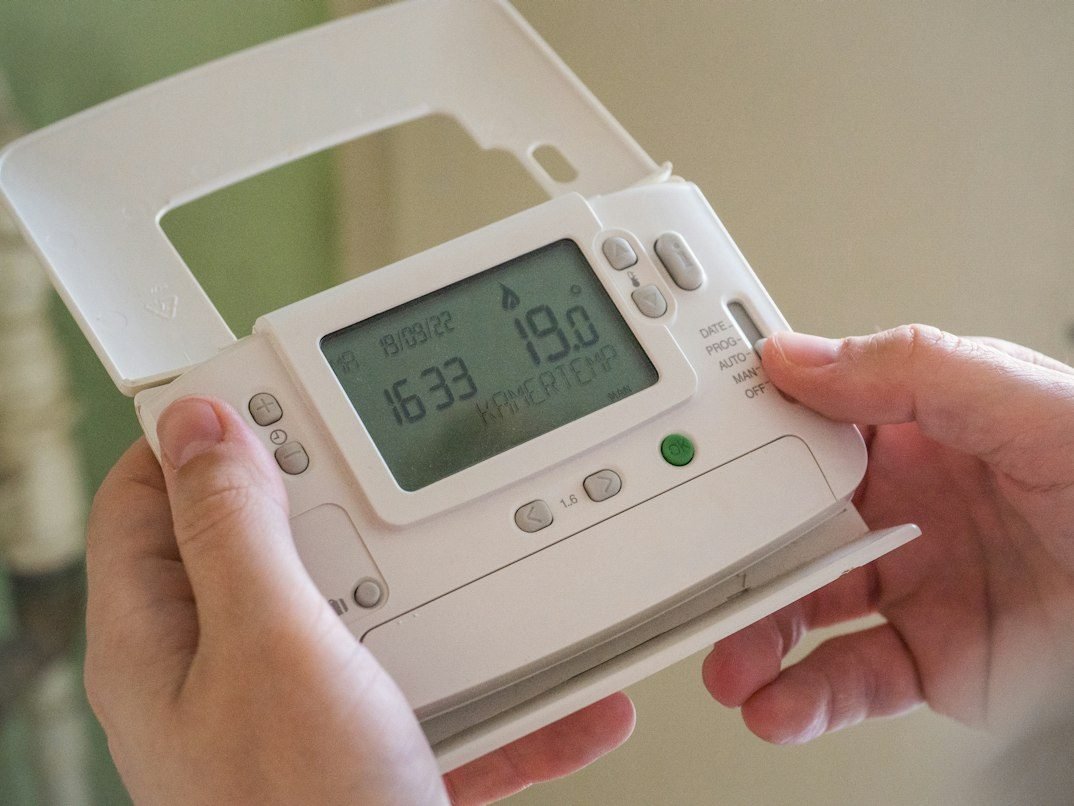 Hands adjusting a white home thermostat set to 19 degrees Celsius.