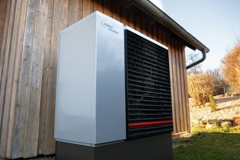 White outdoor heat pump beside a wood-clad home.