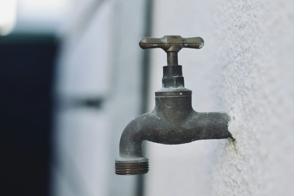 Weathered metal water faucet mounted on a light wall.