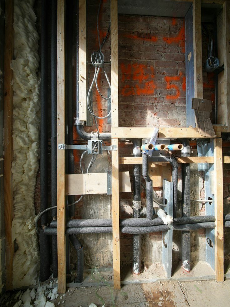 Exposed water pipes and wiring in a home renovation wall.