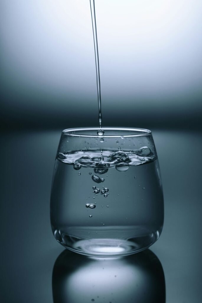 Water pouring into a clear drinking glass on a reflective surface