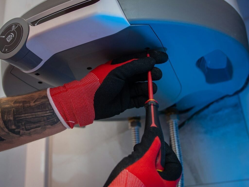 Gloved technician adjusting a wall-mounted water heater with a screwdriver.