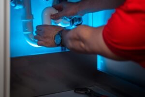 Hands checking white drain-pipe connections inside a sink cabinet