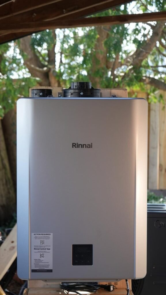 Silver tankless water heater with top vent connections and a front control panel.