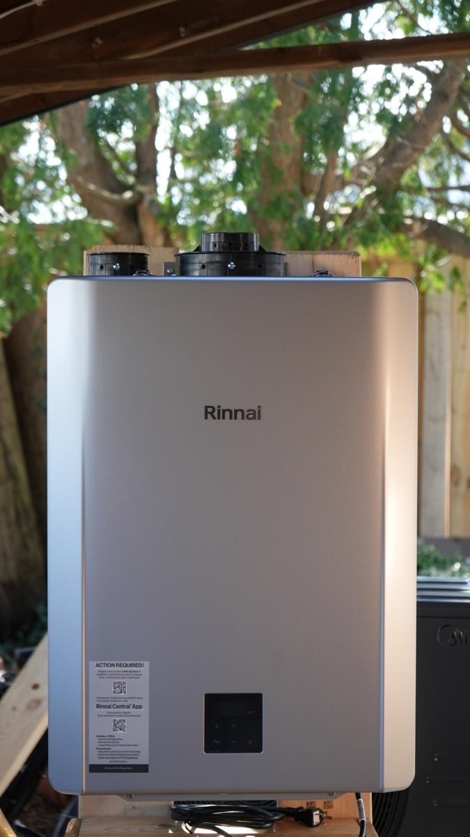 Silver tankless water heater with top vent connections and a front control panel.