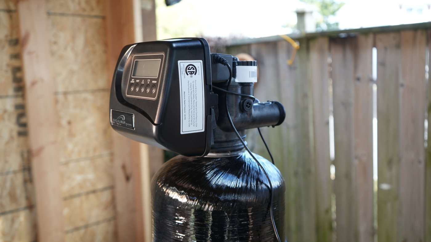Digital control valve and black water treatment tank beside a wooden fence.
